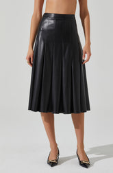 A black leather midi skirt with a high waist, featuring vertical seam details and pleats that create a flared silhouette. The skirt has a smooth, shiny finish and reaches below the knees. The model is wearing it with pointed-toe shoes that have a black and gold chain detail.